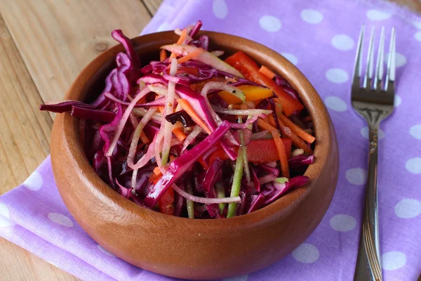 Сырой красный салат из капусты на фиолетовой салфетке с вилкой на деревянном столе — стоковое фото