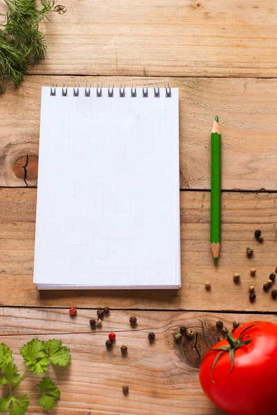 Notebook with green pencil, fresh herbs, spices and tomato on old wooden table in rustic kitchen — Stock Photo, Image