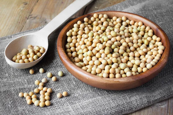 Soybeans in wooden bowl and spoon on linen canvas on wooden table — Stock Photo, Image