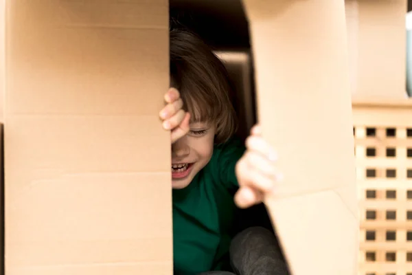 Bonito menino criança jogando em caixa de papelão em nova casa. — Fotografia de Stock