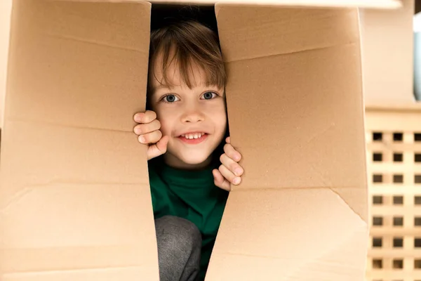 Lindo niño jugando en una caja de cartón en un nuevo hogar. Fotos De Stock