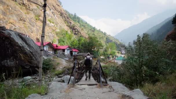 Ein Tourist in den Bergen überquert eine klappbare Brücke über den Fluss. — Stockvideo