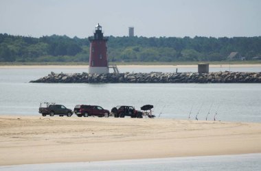 Lewes, Delaware, U.S.A - September 21, 2021 - The view of the fisherman and trucks on Cape Henlopen Beach overlooking the light house clipart