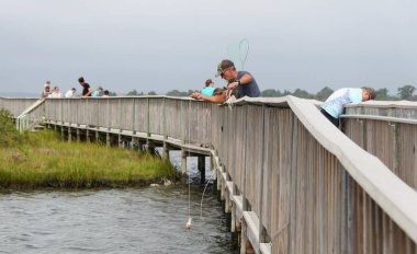 Assateague Adası, Maryland, ABD - 21 Eylül 2021 Köprü üzerinde bir ağ ve ip kullanarak yengeç avlayan bir adam