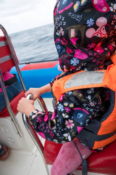 Criança segurando uma cadeira em um barco de velocidade durante o passeio. — Fotografia de Stock