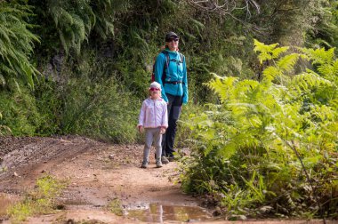 Mother and daughter walking along forest path.