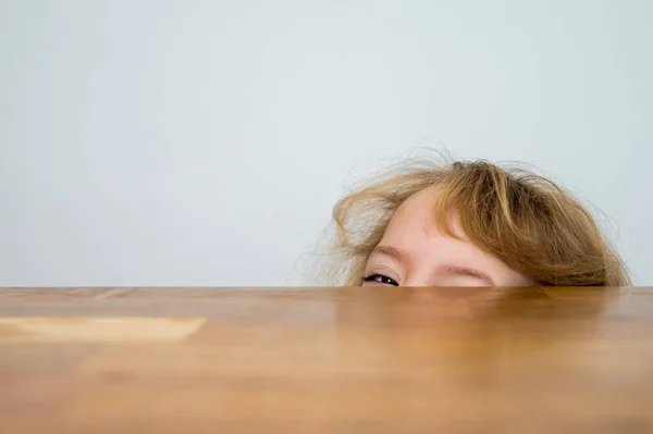 Cute blonde girl hiding half of her face under the wooden table. — Φωτογραφία Αρχείου