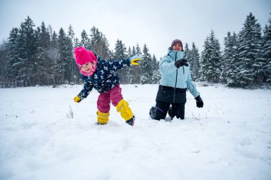 Anne ve kızı kar topu atarak eğleniyorlar..