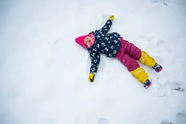 Schattig meisje maken sneeuw engel tijdens de winter. — Stockfoto