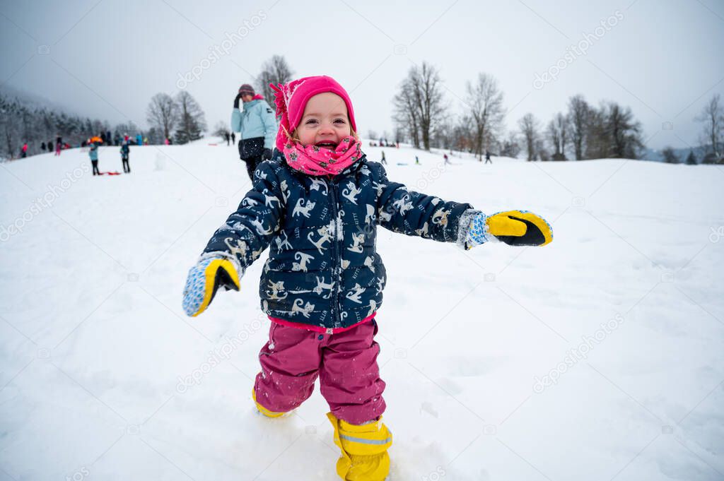 Happy cute girl running down snowy slope.