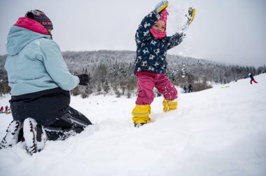 Anne ve kızı karda eğleniyor.