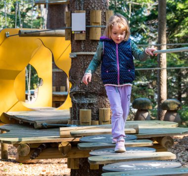 Orman oyun parkında tahta köprüde yürüyen aktif, tatlı bir kız..