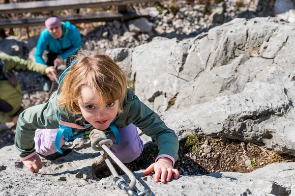 Cute blonde girl rock climbing using top rope with her mother protecting her. — Stock Photo, Image