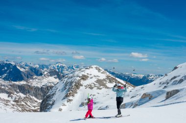 Anne ve kızı dağ tepesindeki bir kayak merkezinde ilk adımlarını atarak eğleniyor ve kayak öğreniyor. Kış boyunca aktif çocukluk.