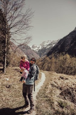 Babası orman çayırında yürürken kızını kucaklıyor. Aktif aile hayatı açık havada.
