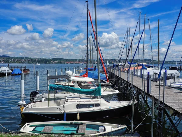 Almanya, Constance Gölü 'nde küçük yelkenli tekneleri olan ahşap bir gemi iskelesi. Mavi yaz gökyüzü beyaz renkli bulutlarla.