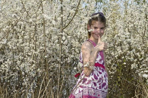 Menina com flores brancas atrás do arbusto mostrando OK — Fotografia de Stock