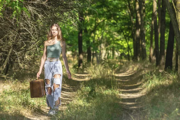 若いです女性歩くで森林未舗装道路とともに古い茶色のスーツケース — ストック写真