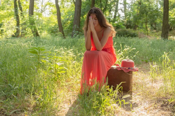 Jovem Mulher Vestido Vermelho Sentado Velha Mala Marrom Orando Bosques — Fotografia de Stock