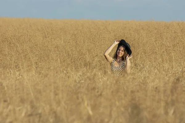 黒い帽子をかぶった若い女性が晴れた日に小麦畑に覆われています — ストック写真