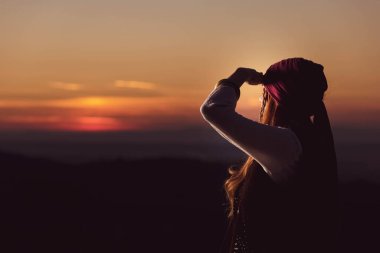 Gün batımına bakan korsan kostümlü genç bir kadının açık hava portresi.