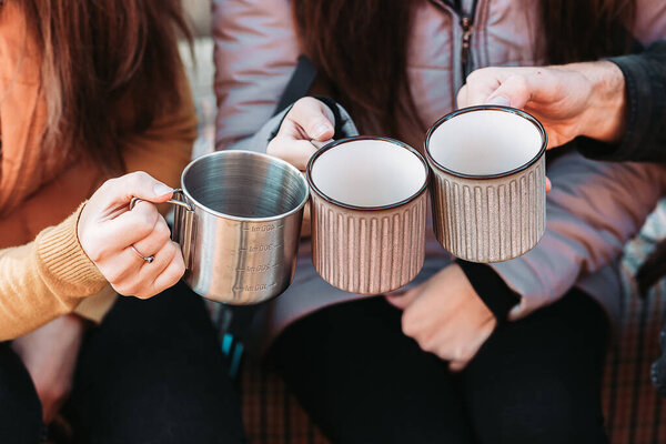 Close-up of three friends holding metal travel mugs with.