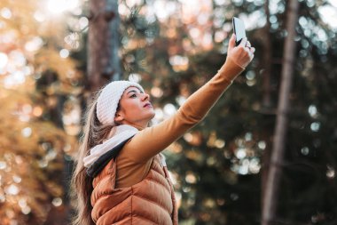 Genç, esmer kadın ormanda telefon sinyali yakalıyor.