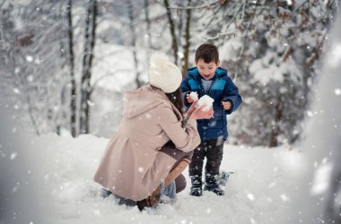 Young, beautiful mom and her cute little boy playing in the snow, making snowball