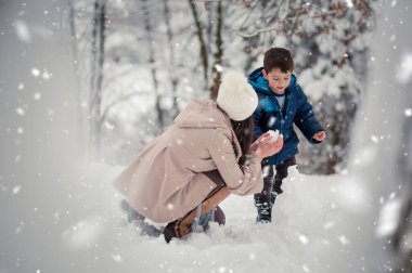 Young, beautiful mom and her cute little boy playing in the snow, making snowball