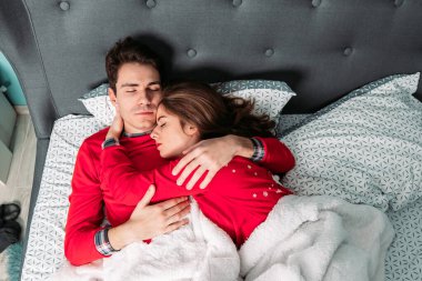 Kırmızı pijamalarıyla yatakta yatan, sarılan ve mutlu görünen çift..