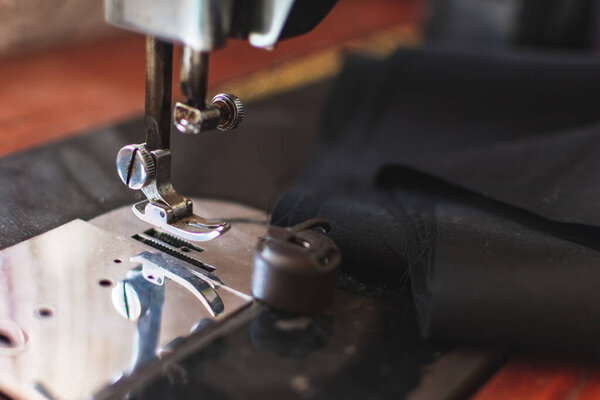 Close-up photo of sewing machine with black piece of fabric. Fashion design concept