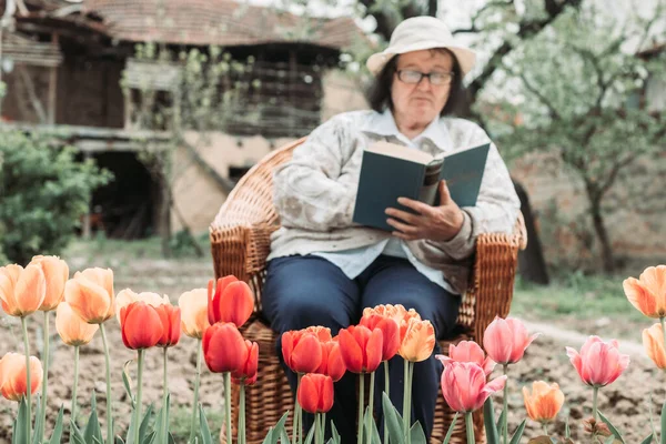 Starší Žena Odpočívá Čte Zahradě Tulipány Před — Stock fotografie