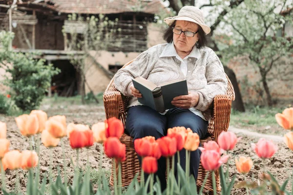Starsza Kobieta Relaksuje Się Czyta Książkę Ogrodzie Tulipany Przed Nią — Zdjęcie stockowe