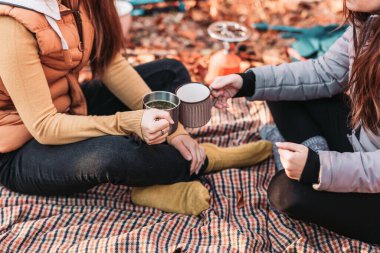 Two girls drinking hot tea from metal cups outdoor, camping