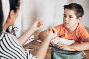Little school boy doing homework with his mom helping him with assignments