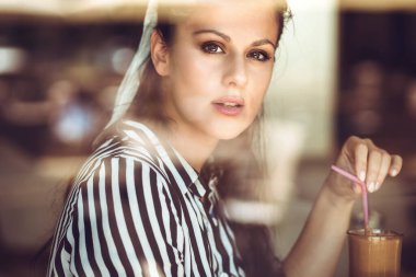 Kafe penceresinden kahve içen bir kadının portresi.