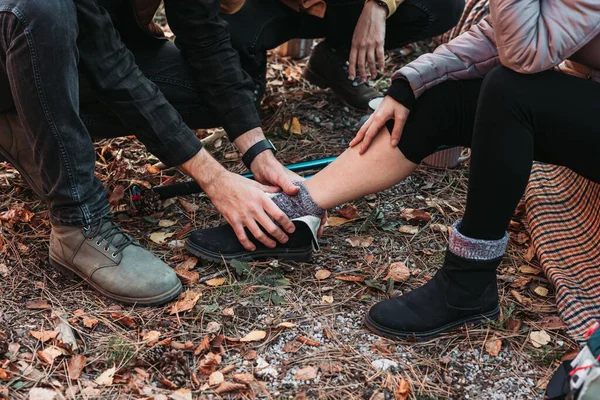 Young woman sprained her ankle while hiking. Her friends are helping her