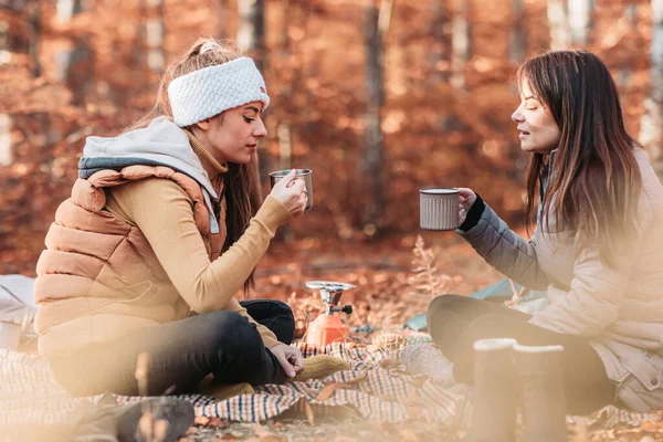 Two girls drinking hot tea from metal cups outdoor, camping
