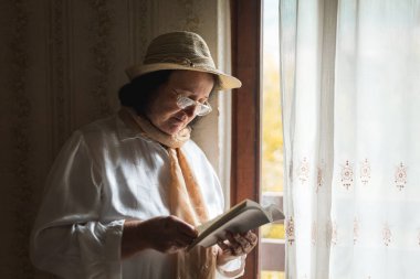Pencerenin yanında kitap okuyan yaşlı bir kadın.