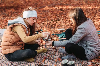 Two girls drinking hot tea from metal cups outdoor, camping