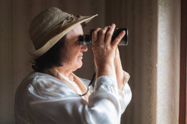 Yaşlı kadın dürbünden bakıyor, gözetliyor.