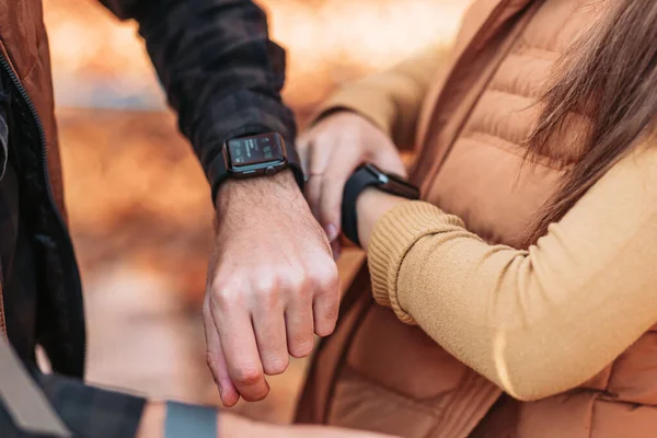 Male and female hands with smart watches. Outdoors, autumn colors