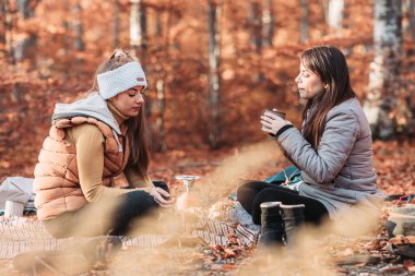 Two girls drinking hot tea from metal cups outdoor, camping
