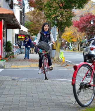 Karuizawa, Japonya - 7 Kasım 2019. Japonya, Karuizawa 'da sokakta bisiklet süren bir kadın. Karuizawa, Nagano dağlarında sonbahar doğasıyla ünlü bir tatil beldesidir..