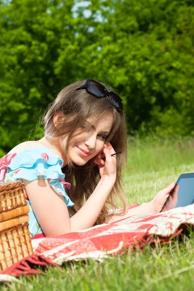 Beautiful woman enjoys the tablet at a picnic — Stock Photo, Image