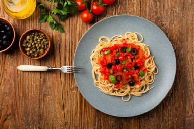 Domates ve zeytinli İtalyan spagetti alla Pultanesca. Et ve peynir olmadan servis edilir. Üst Manzara. Doğal ahşap zemin. 