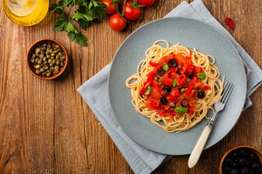 Domates ve zeytinli İtalyan spagetti alla Pultanesca. Et ve peynir olmadan servis edilir. Üst Manzara. Doğal ahşap zemin. 