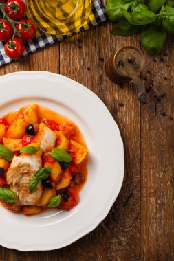 Geleneksel ispanyolca morina balığı. Domates sosunda haşlanmış patates, olivki ve fesleğen ile servis edilmiş. Üst görünüm. 