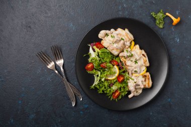 Mantar soslu kızarmış morina balığı ve salata. Siyah bir tabakta porsiyon. Koyu arkaplan.