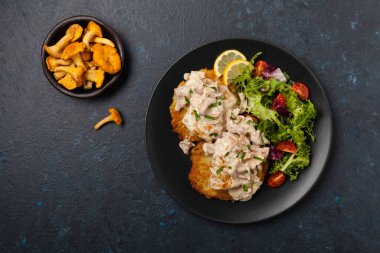 Kızarmış morina, patatesli krep, mantar sosu ve salata ile servis edilir. Siyah bir tabakta porsiyon. Koyu arkaplan.